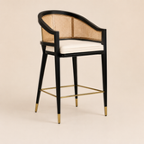 Levanto Kitchen Bar Stool Chair in black wood with natural rattan backrest, cream upholstered seat and brass accents in a luxury beige kitchen interior.
