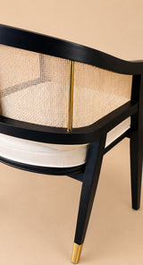 Levanto Dining Chair in black wood with natural rattan backrest and cream upholstered seat in a luxury dining interior.
