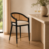 Levanto Kitchen Bar Stool Chair in black wood with natural rattan backrest, cream upholstered seat and brass accents in a luxury beige kitchen interior.