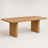 A minimalist rectangular wooden table with rounded corners and thick blocky legs, shown on a clean off-white background.
