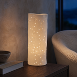 Malmo Small white ceramic luminary glowing in a blue-hour reading corner