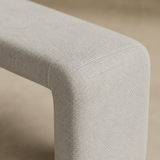 Close detail of the Veneziana bench fine stone-ivory woven upholstery and rounded waterfall transition into one end-panel support