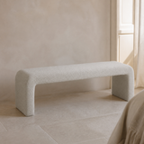 Veneziana continuous waterfall bench in fine stone-ivory woven upholstery with exactly two broad end-panel supports, premium Mediterranean lifestyle view