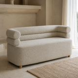 Vernazza compact sofa in fine gray-ivory woven fabric with monolithic base, continuous seat, exactly two stacked rounded bolster rails curving into both arms and low wooden ball feet, alternate lifestyle
