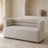 Vernazza compact sofa in fine gray-ivory woven fabric with monolithic base, continuous seat, exactly two stacked rounded bolster rails curving into both arms and low wooden ball feet, premium lifestyle