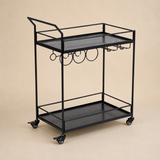 Walker all-black two-tier iron bar cart with raised handle, hanging bottle and stemware racks and four caster wheels in a warm beige studio